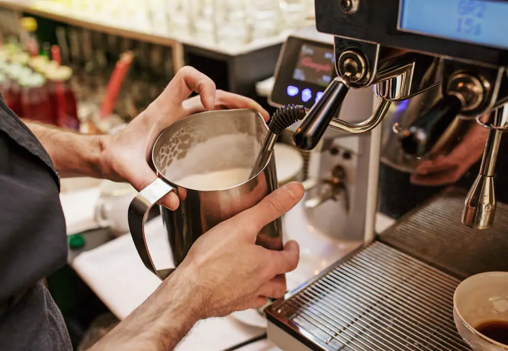barista holding metal jug while steaming the milk