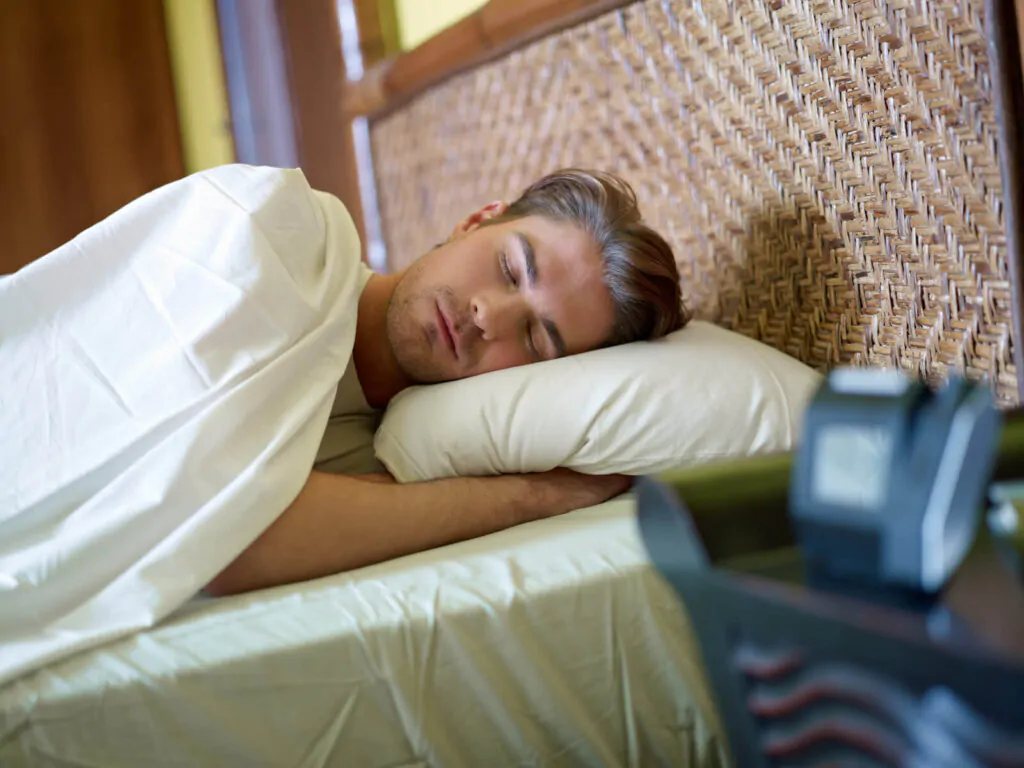 serene caucasian adult man lying in bed with alarm clock in foreground