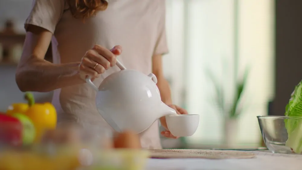 Woman pouring tea into cup on kitchen
