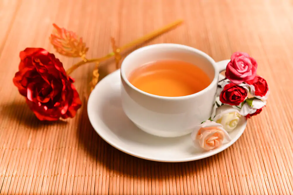 a cup of rose tea with rose petals and buds surrounding