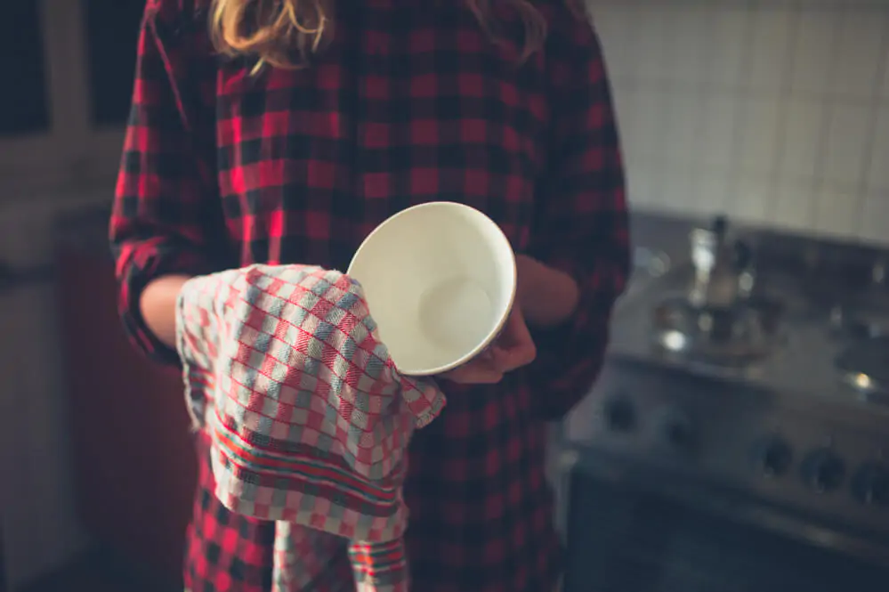 A young woman is drying the dishes using a tea towel - What is a tea towel