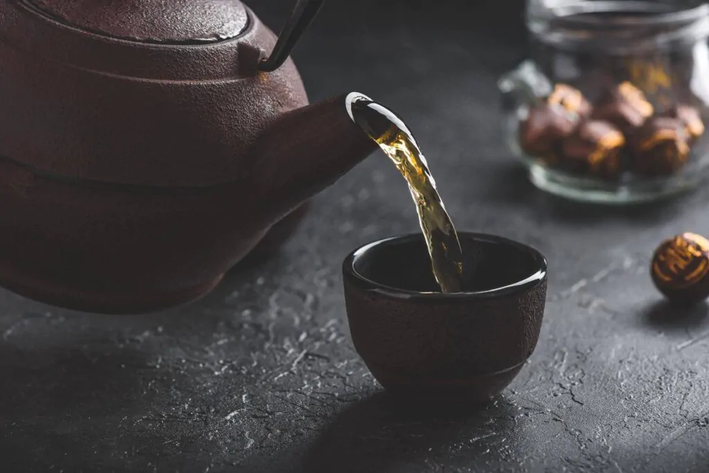 Pouring ready green tea from iron kettle into tea bowl