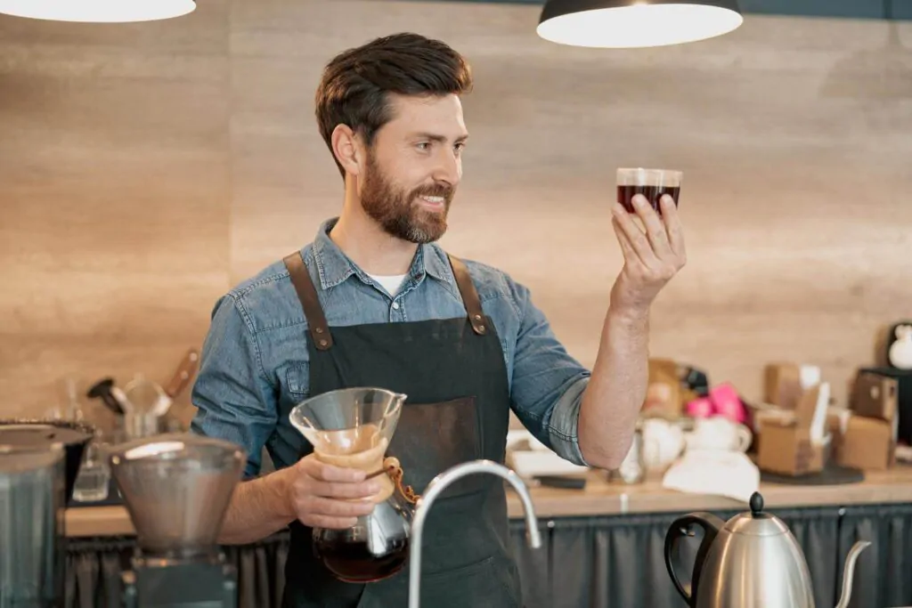 Smiling barista appraisingly looks at a glass of filter coffee - How to be a good barista