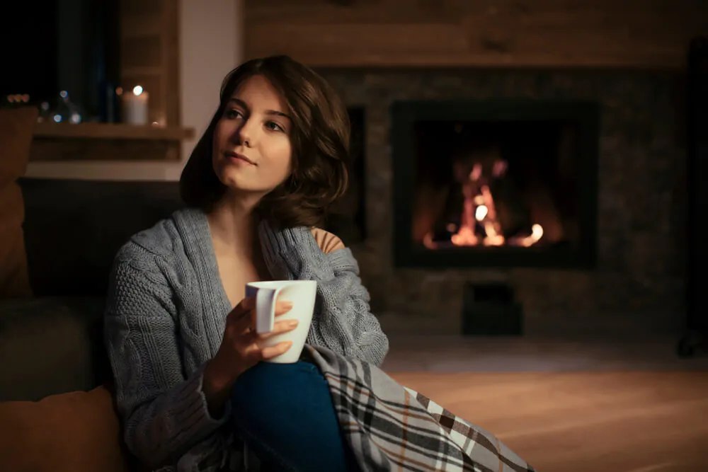 beautiful Caucasian woman sitting by the fireplace in cozy sweater and drinking tea - What is the best tea to drink at night