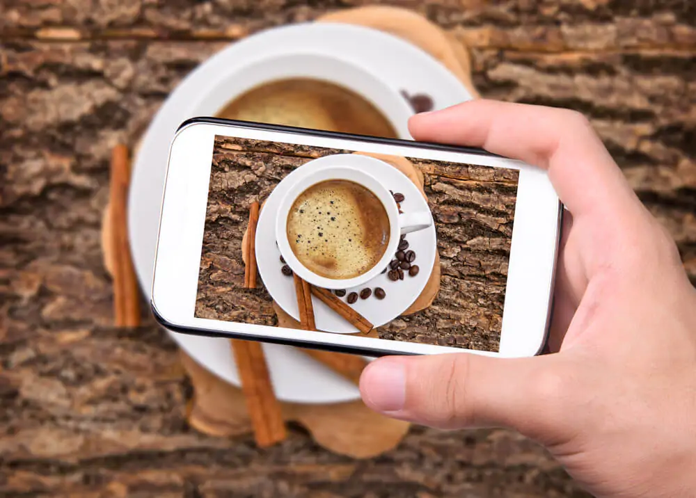 Hands taking photo coffee cup with smartphone - how to market your coffee online