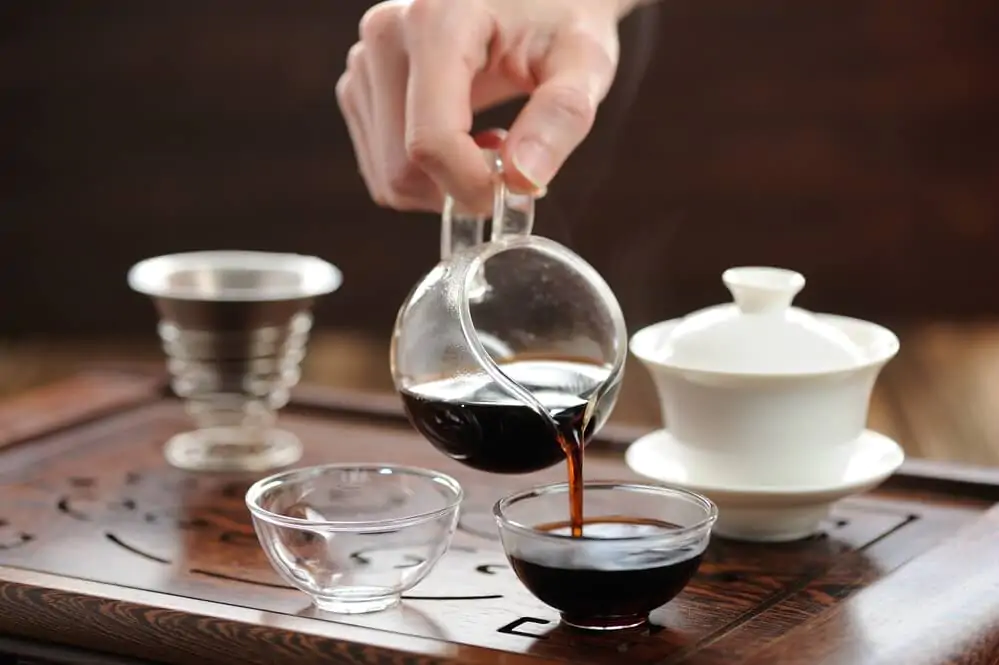 a hand holding pu-erh tea while pouring it in a mini mug