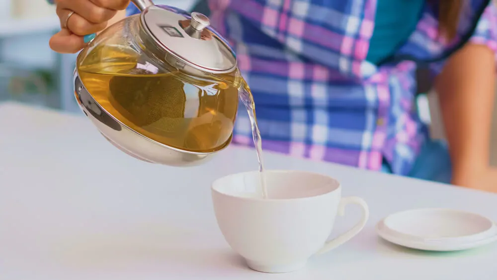 woman holding a hot tea while pouring it in a cup