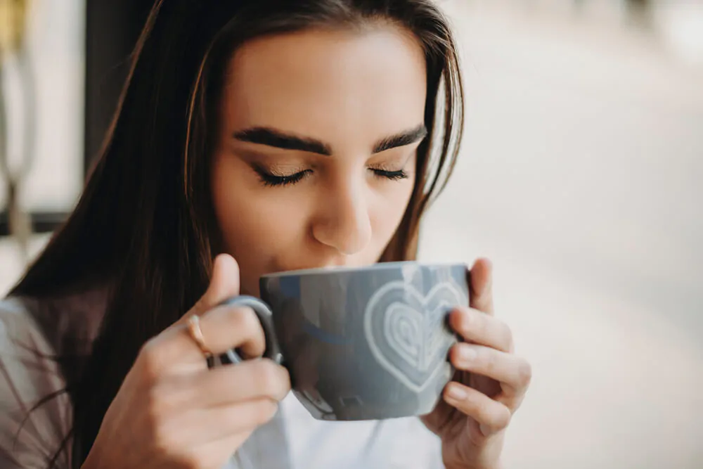 woman closing her eyes while sipping her cup of coffee