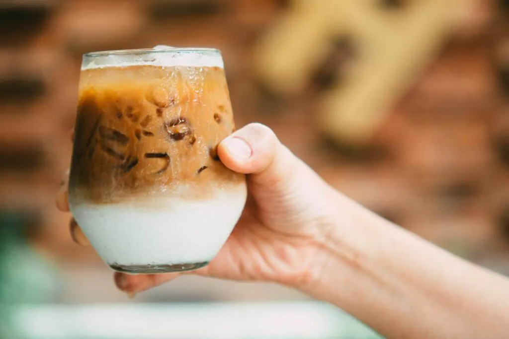 holding iced latte coffee in a glass with cream on bottom - iced coffee alternatives