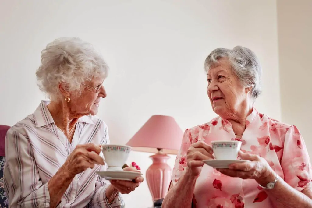 two elderly women holding both cup of tea while talking