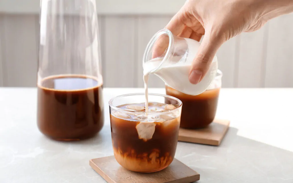 Woman pouring milk into glass with a hard cold brew coffee recipes on table