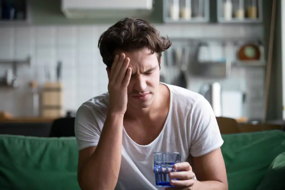 man touching his forehead after drinking from a glass cup - why tea is dehydrating