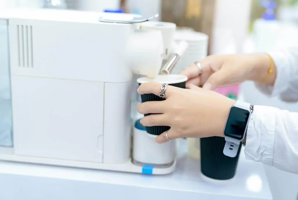  Woman holding a black cup taking coffee from a smart coffee machine on the table