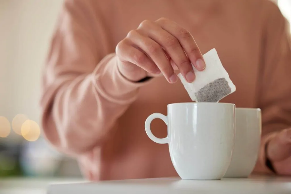 A woman dropping a tea bag into a waiting mug