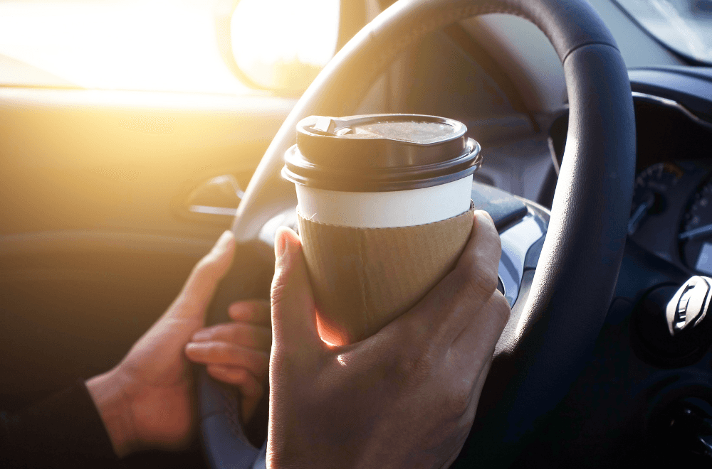 Woman holding her cup of coffee and steering wheel