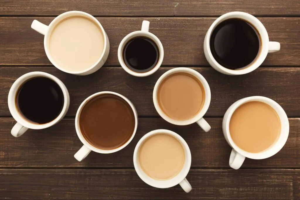 Different types of coffee in cups on wooden table, top view