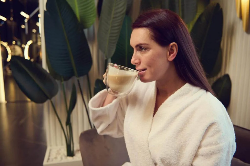 Woman in white terry bathrobe drinking cappuccino