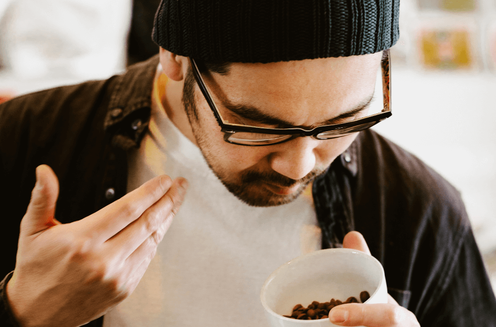 A man smelling coffee beans in a plastic cup
