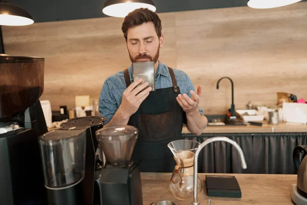 Handsome barista enjoys the great aroma of coffee beans at his workplace