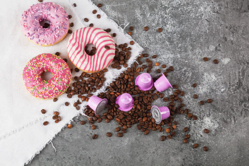 Espresso pink plastic capsules with foil and coffee beans and sweet donuts