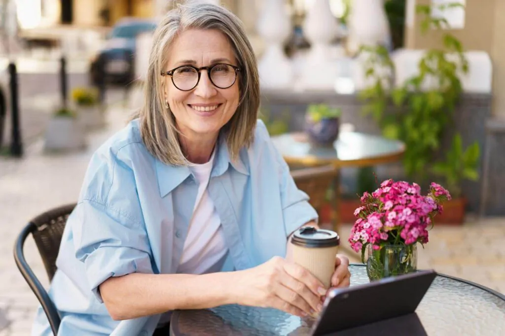 Grey hair charming woman drinking coffee  sitting at a table in a street cafe