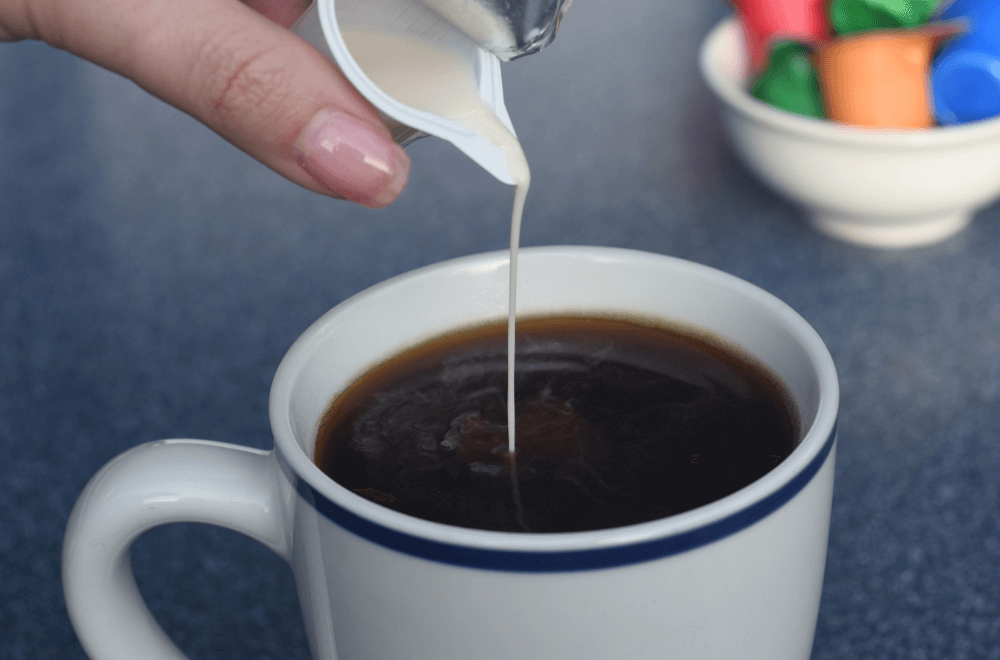 Pouring liquid creamer in a cup of coffee