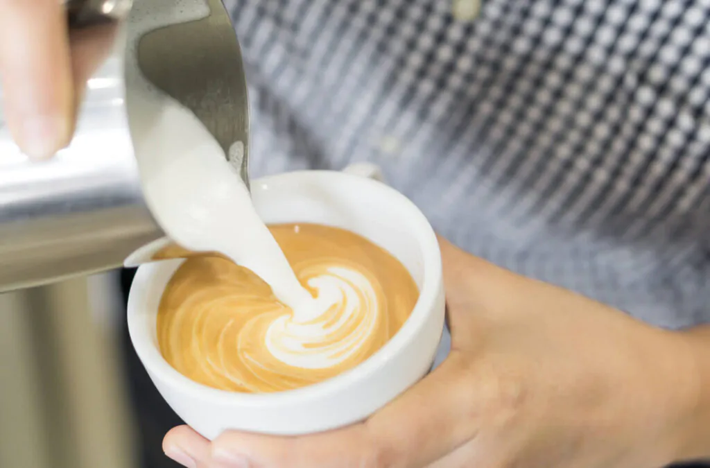 Woman barista pouring stream milk for making latte art coffee in