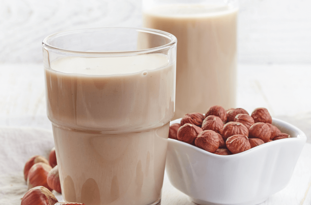 A glasses of hazelnut milk with bowl of hazelnut beside