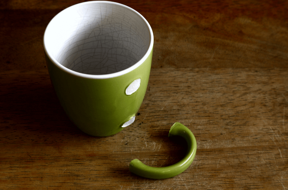 A green ceramic mug with a broken handle on a wooden table