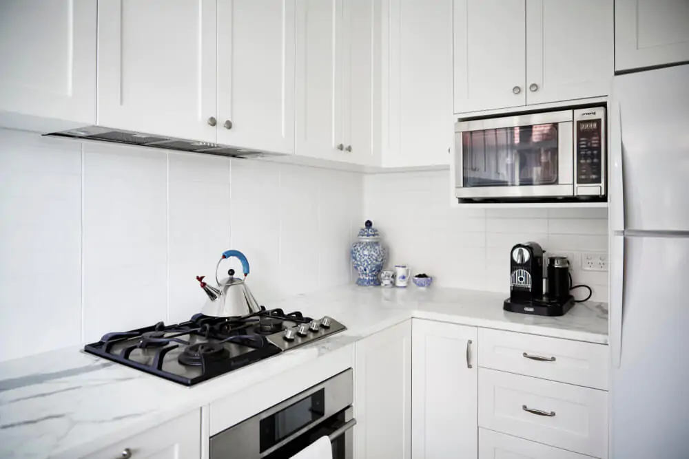 A modern white kitchen with a marble bench top, stainless steel appliances and a kettle
