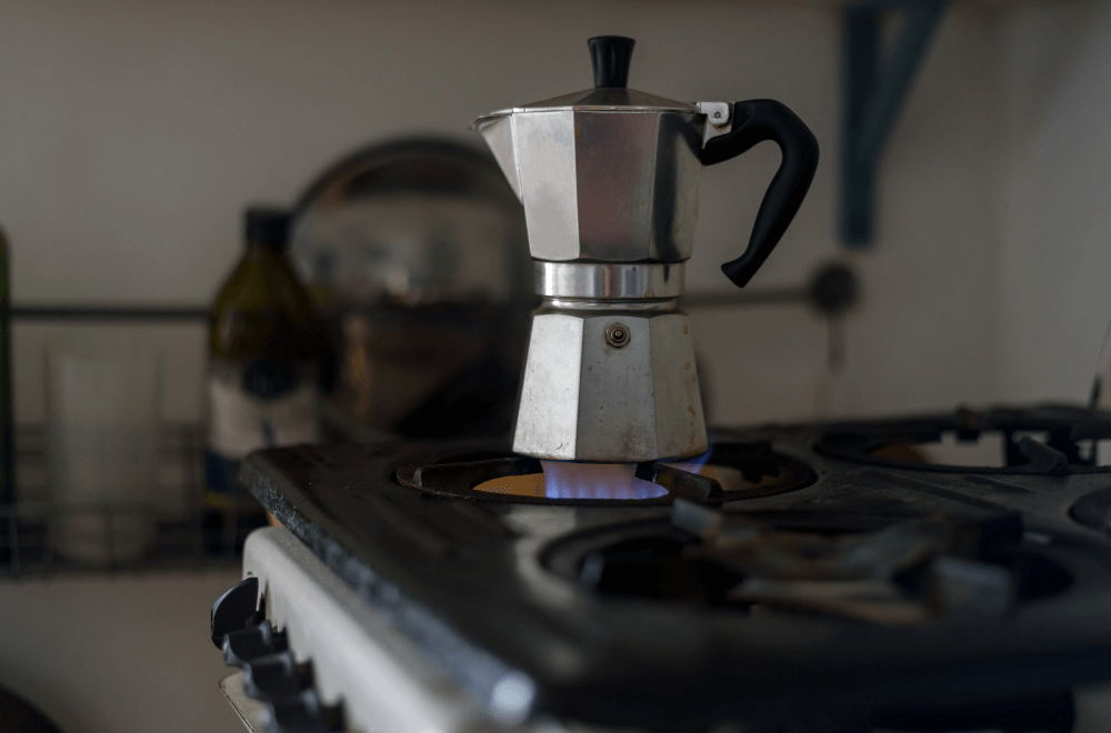 A little worn Italian coffee pot on a gas stove in a kitchen.