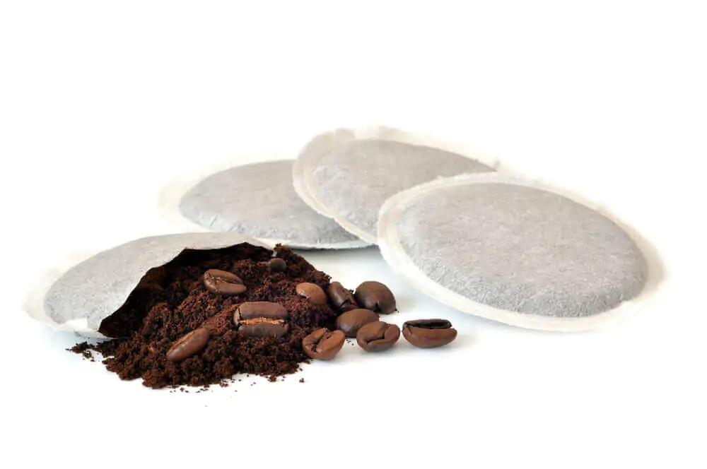 Four white coffee pods with the contents of one pod exposed.