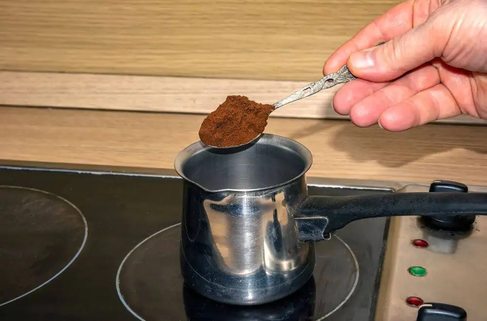 hand putting coffee with a spoon in the empty pot on the stove