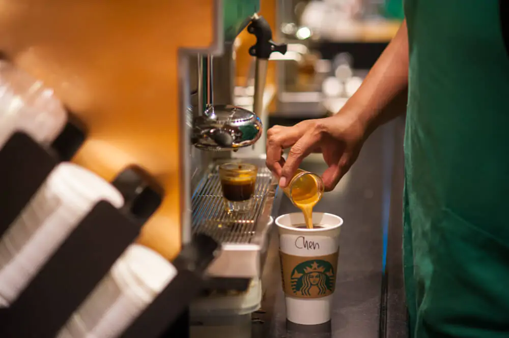 Close up of a Starbucks Coffee Barista is standing in front coffee machine and making an americano coffee for customers