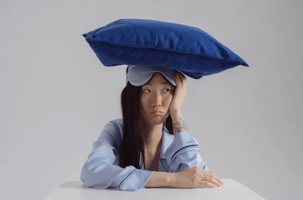 A woman in light blue long sleeves with a pillow on her head