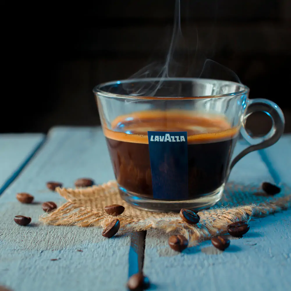 An espresso Lavazza glass cup with coffee beans around
