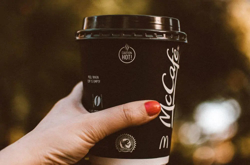 A woman's hand holding out a McCafe cup of coffee