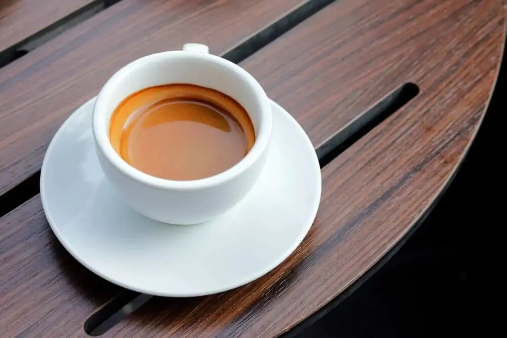 A cup of coffee was placed on top of a white saucer on a wooden table