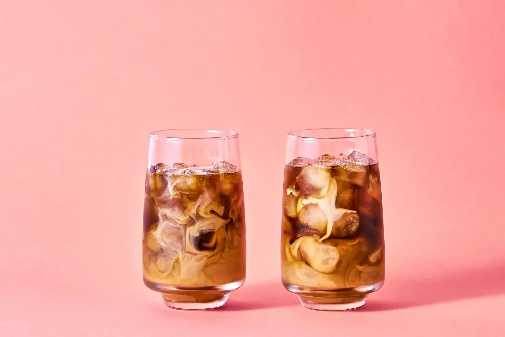 Iced coffee with milk in tall glasses on pink background
