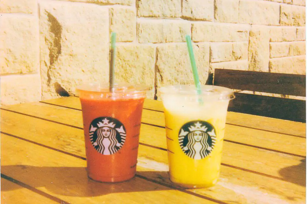 Orange and yellow Starbucks juices in plastic cups with lids and straw
