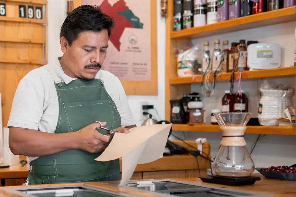 An Hispanic barista is cutting a paper filter to make coffee