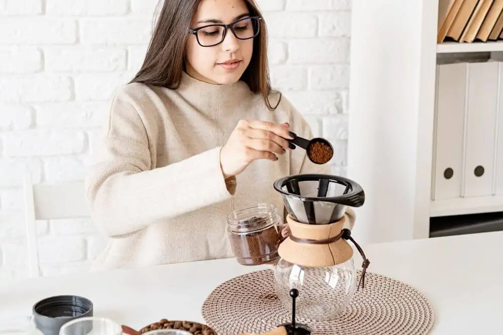Woman brewing coffee in Chemex pouring grinded coffee beans into filter