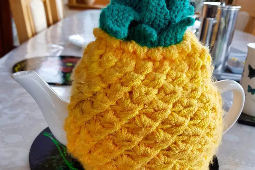 A knitted pineapple is used as a tea warmer for a teapot