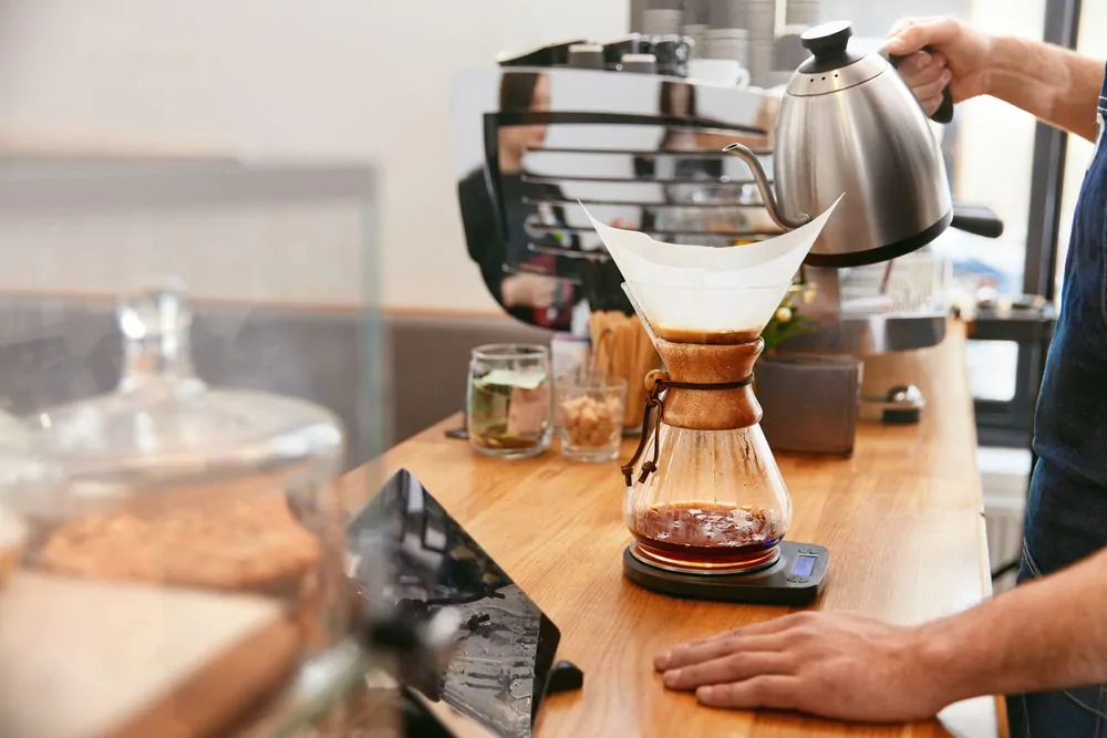 Barista holding a hot kettle while using pour-over coffee maker