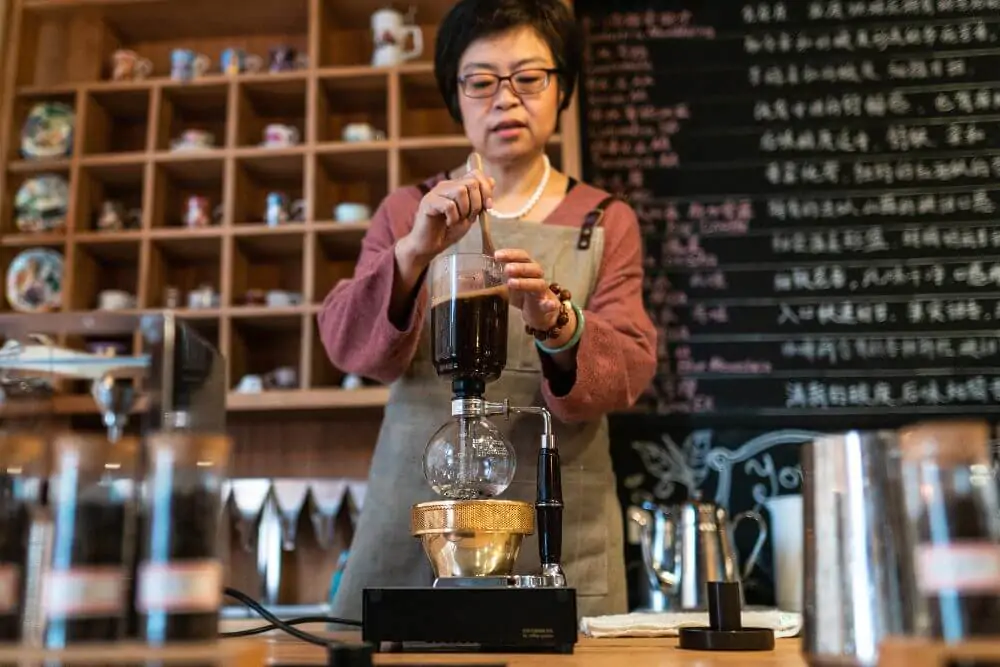 Mature woman using a siphon coffee maker in coffee lab