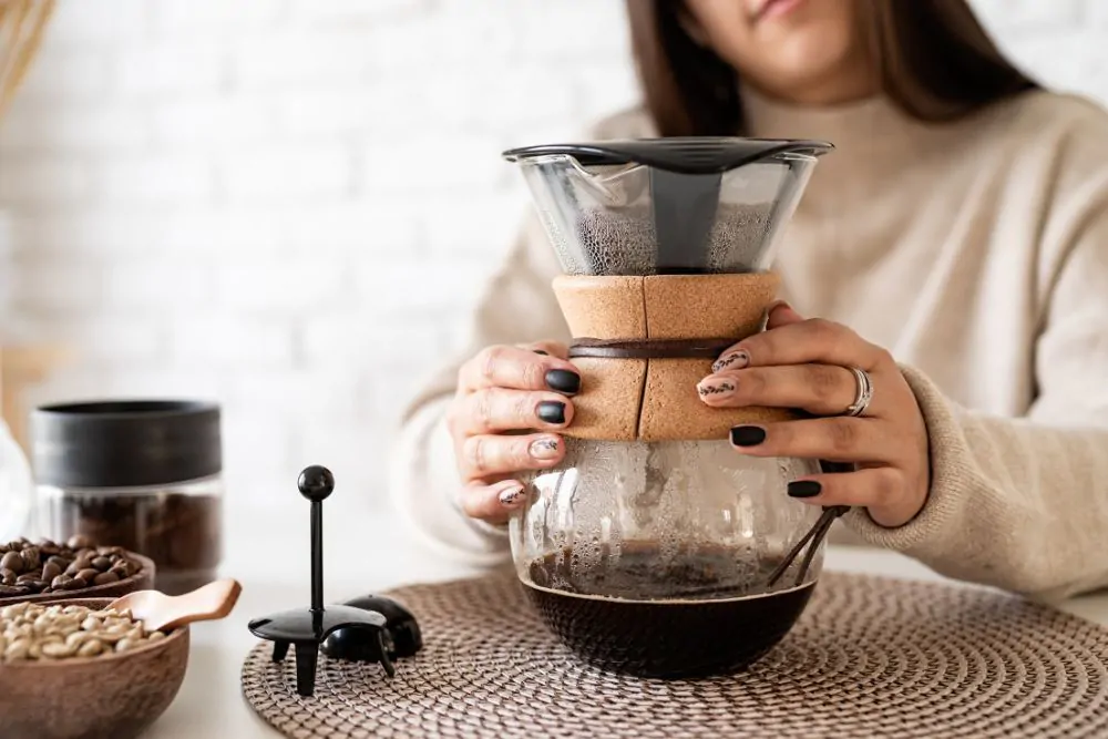 Young woman brewing coffee in chemex, pouring hot water into the filter