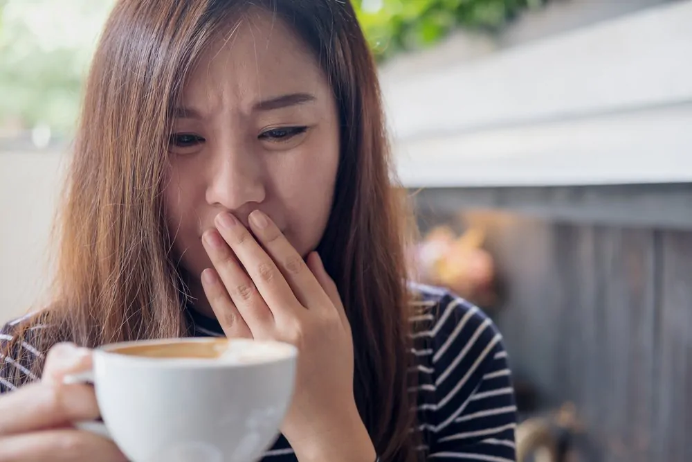 A woman holding hot coffee with feeling strange and smelling bad in coffee shop