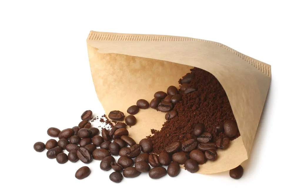 Filter with ground coffee and coffee beans on white background