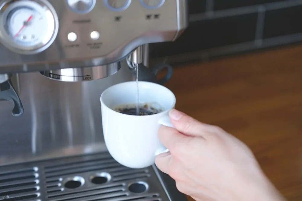Pouring hot water into a cup of freshly brewed espresso close-up as an additional optional function of the espresso machine
