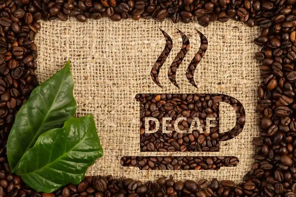 Cup with decaf text written as aroma of no-caffeine hot beverage inside scattered coffee beans frame on brown burlap bag background